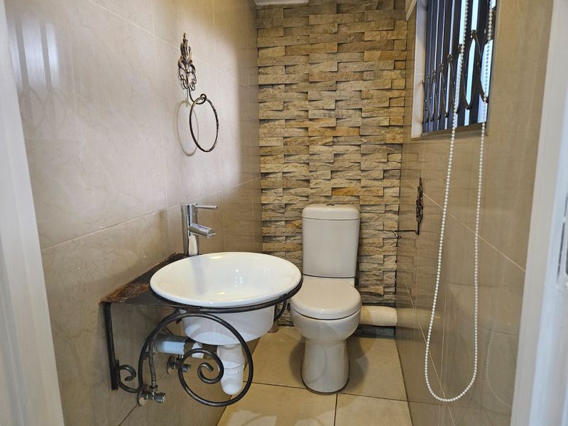 A compact guest bathroom featuring a wall-mounted basin, ceramic toilet, and a decorative stone-clad feature wall.