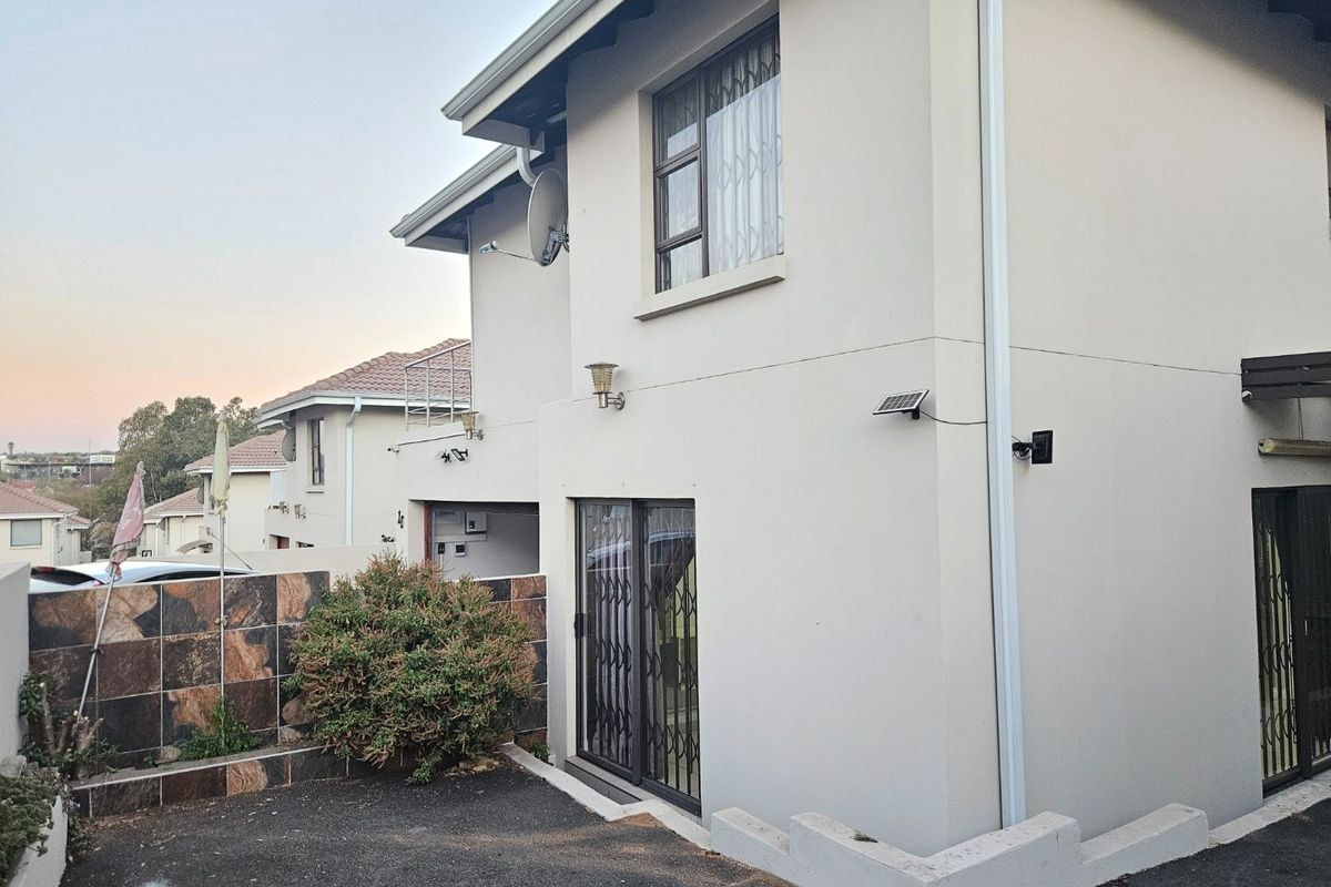 Rear view of the townhouse featuring a paved area, sliding glass door with security gate, and exterior wall-mounted lighting.