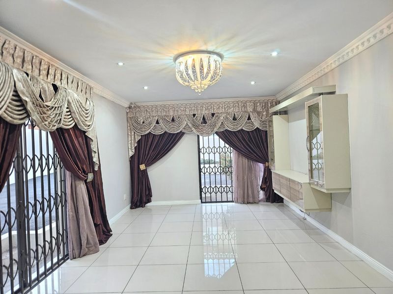 Spacious living area featuring polished porcelain floor tiles, a built-in wall unit, decorative ceiling cornices, and secure metal gates leading to the exterior.