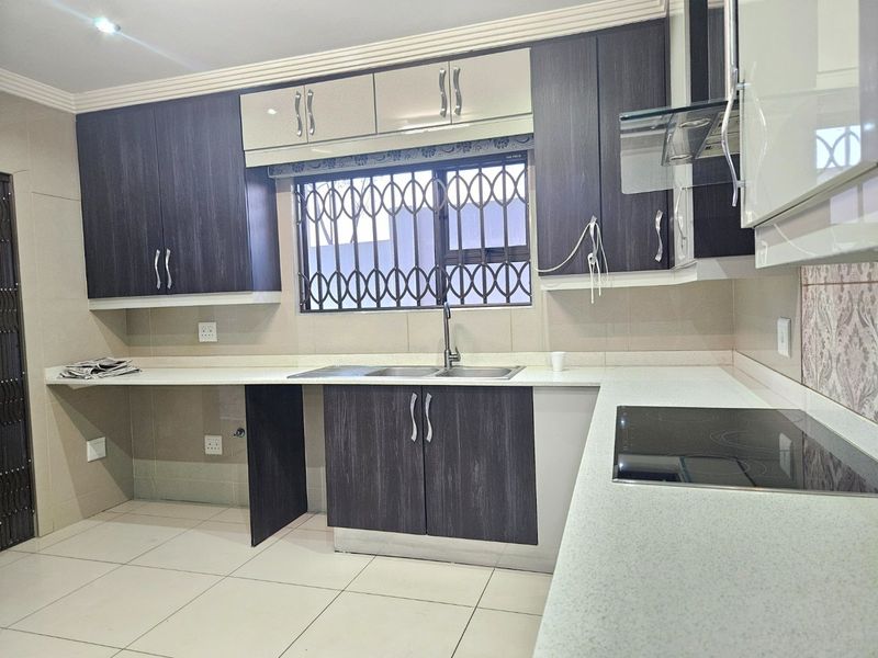 Modern kitchen featuring dark wood-grain cabinetry, light stone countertops, integrated electric hob, extractor fan, and tiled flooring with a secure window.