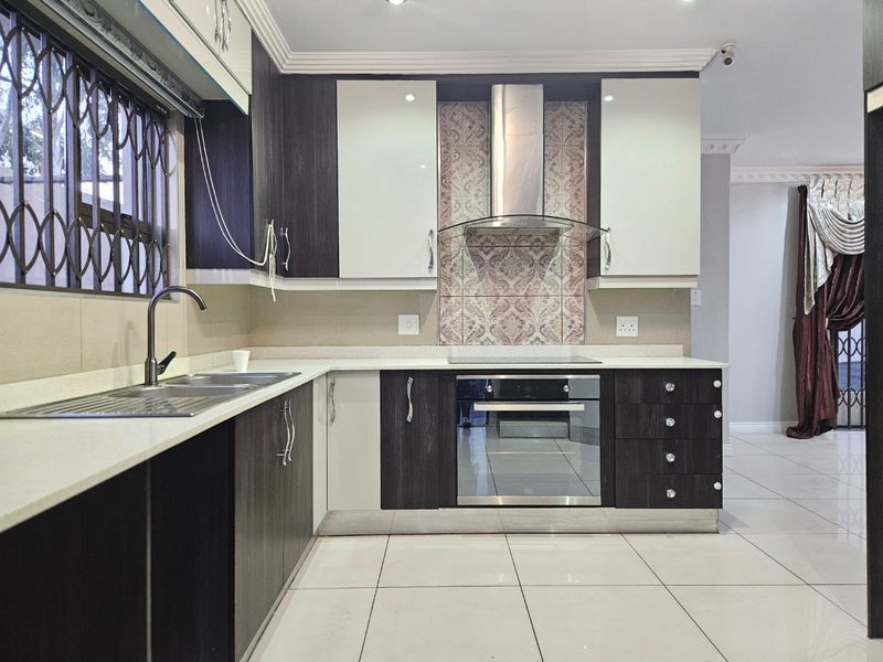 Modern kitchen featuring two-tone cabinetry, integrated oven and hob, extractor fan, and tiled flooring with a clean, contemporary finish.