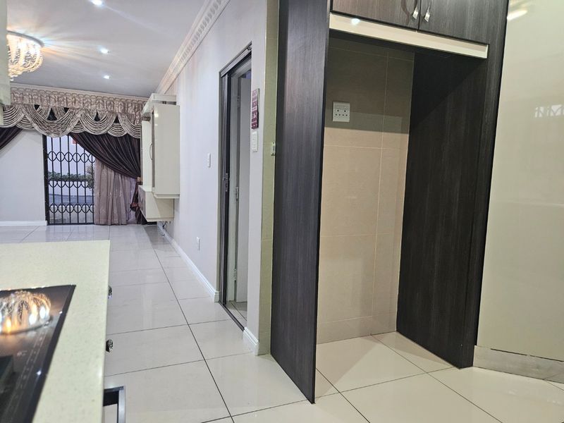 A clean kitchen area featuring tiled flooring, built-in cabinetry, and recessed lighting, with a dedicated space for a refrigerator and access to a security gate.