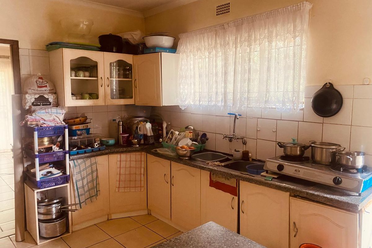 A functional kitchen featuring laminate cabinetry, granite countertops, a double basin sink, and tiled backsplash, offering potential for modernization.