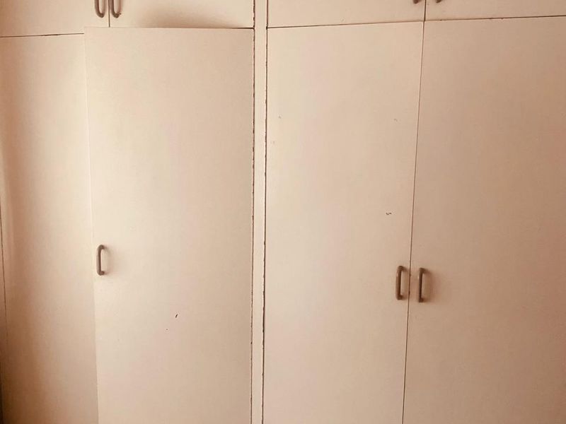 A bedroom featuring built-in cupboards with tiled flooring, showing signs of wear and a misaligned door requiring maintenance.