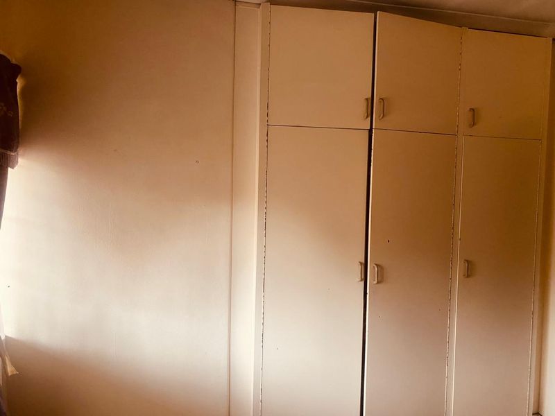 A bedroom interior featuring dated built-in cupboards with a plain wall finish.