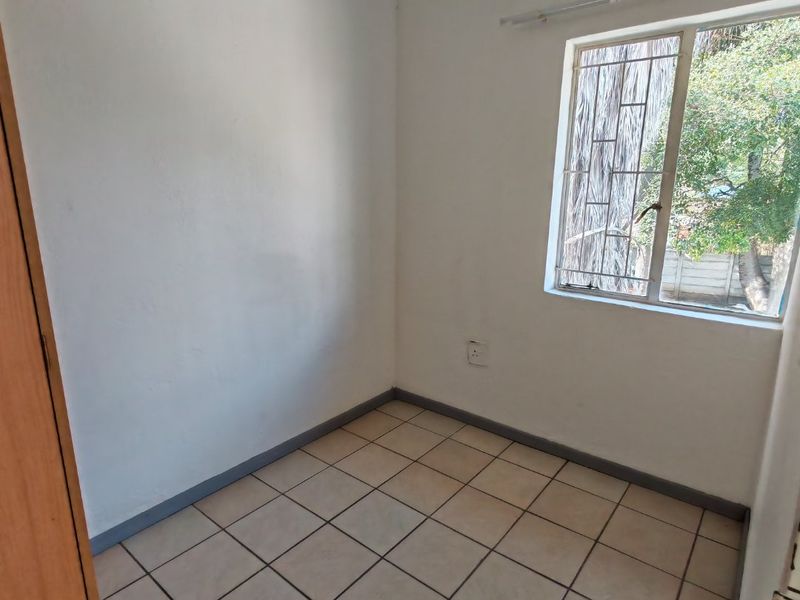 An empty bedroom featuring tiled flooring, a built-in cupboard, and a window fitted with security bars.
