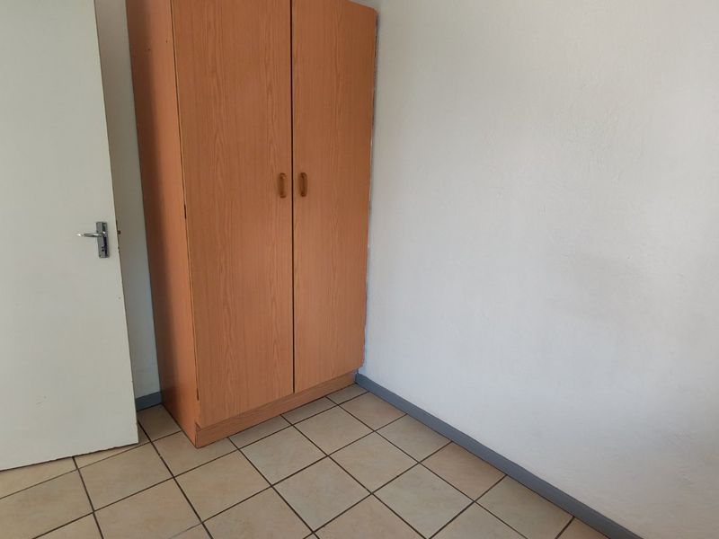 A bedroom featuring tiled flooring and a built-in wooden wardrobe, providing a functional and neutral space ready for personalization.