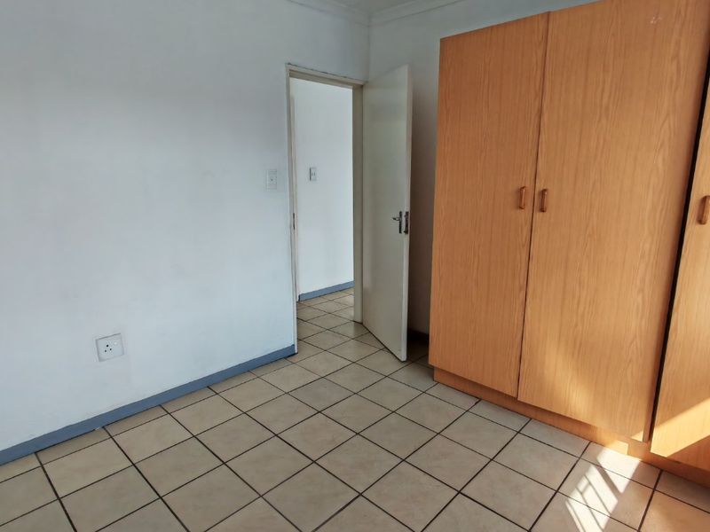 A simple bedroom featuring tiled flooring, a built-in wooden wardrobe, and a neutral interior finish.