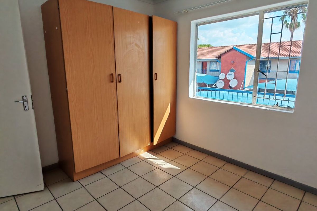 A bedroom featuring tiled flooring, a built-in wooden wardrobe, and a window fitted with security bars, offering a functional and well-lit living space.