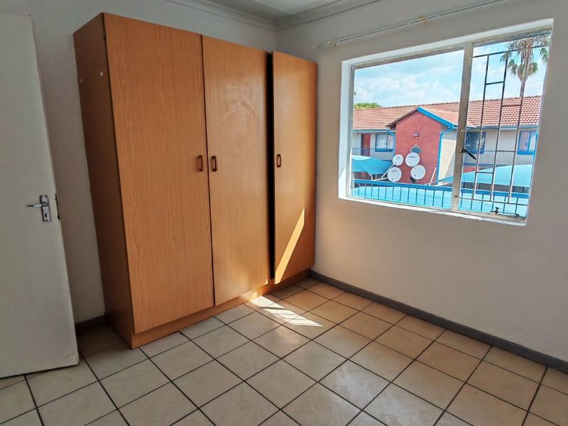 A bedroom featuring tiled flooring, a built-in wooden wardrobe, and a window fitted with security bars, offering a functional and well-lit living space.