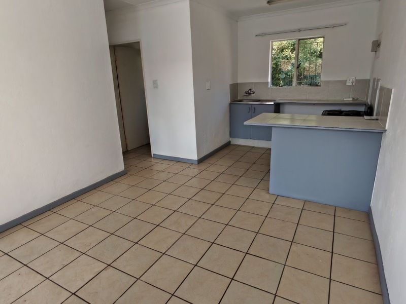 An open-plan kitchen and living area featuring tiled flooring, built-in cabinetry, a breakfast bar, and a hob, presenting a blank canvas for renovation.