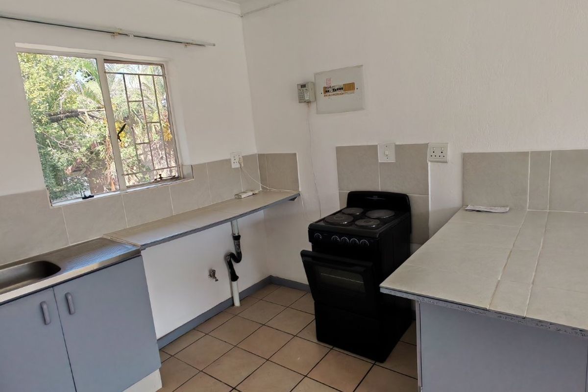 A functional kitchen featuring tiled flooring, built-in cabinetry, a stainless steel sink, and a freestanding electric stove with tiled splashbacks.