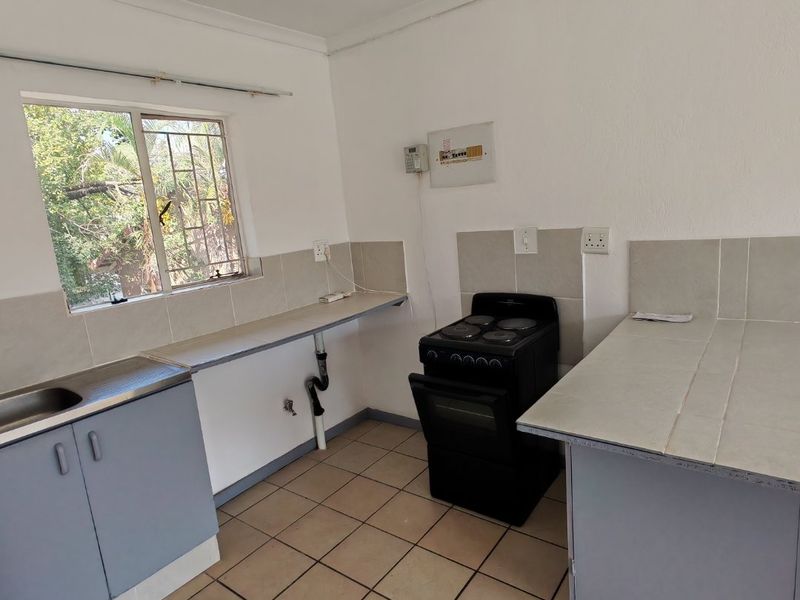 A functional kitchen featuring tiled flooring, built-in cabinetry, a stainless steel sink, and a freestanding electric stove with tiled splashbacks.
