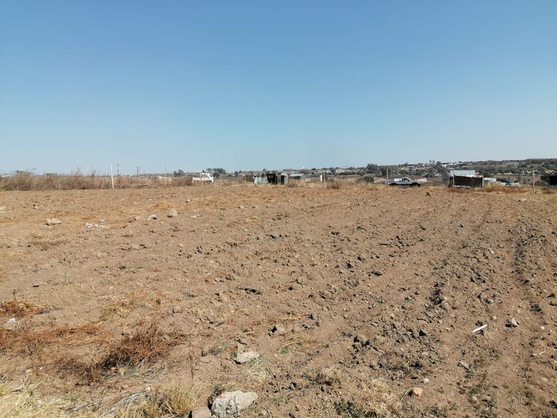 A wide-angle view of a vacant residential plot of land with cleared soil and distant boundary fencing.