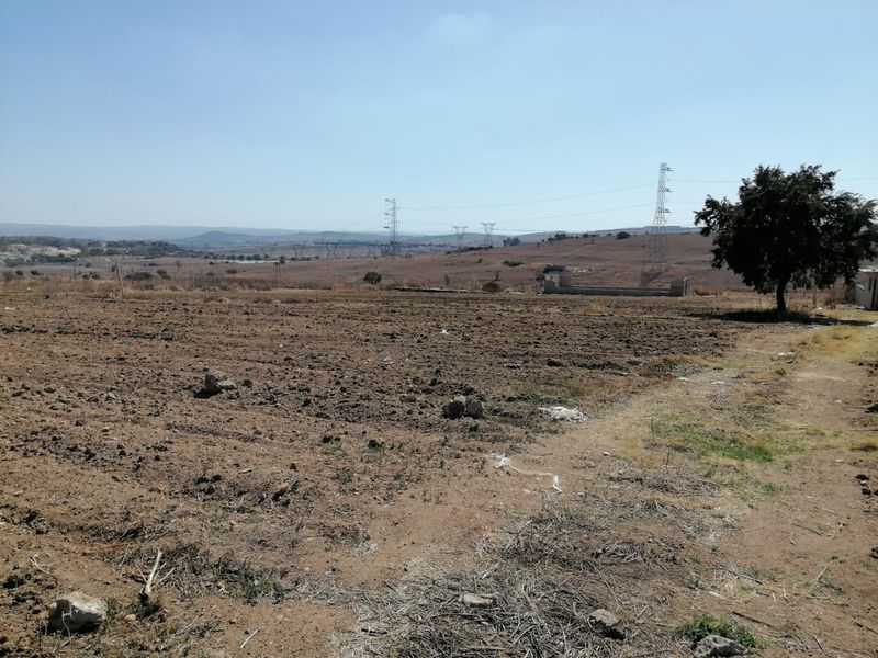 A wide-angle view of a vacant residential plot featuring open land, distant power lines, and a partial boundary wall.