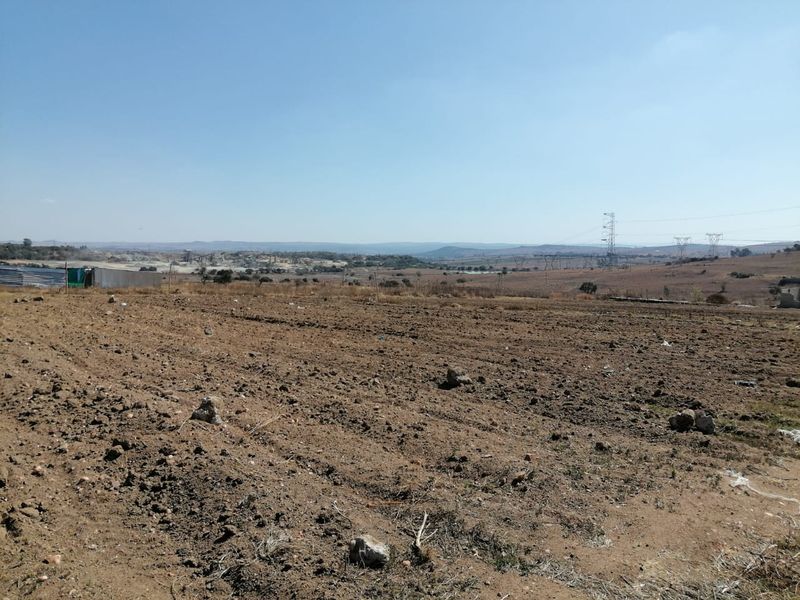 A wide-angle view of a vacant residential plot featuring open, undeveloped land with a distant landscape horizon.
