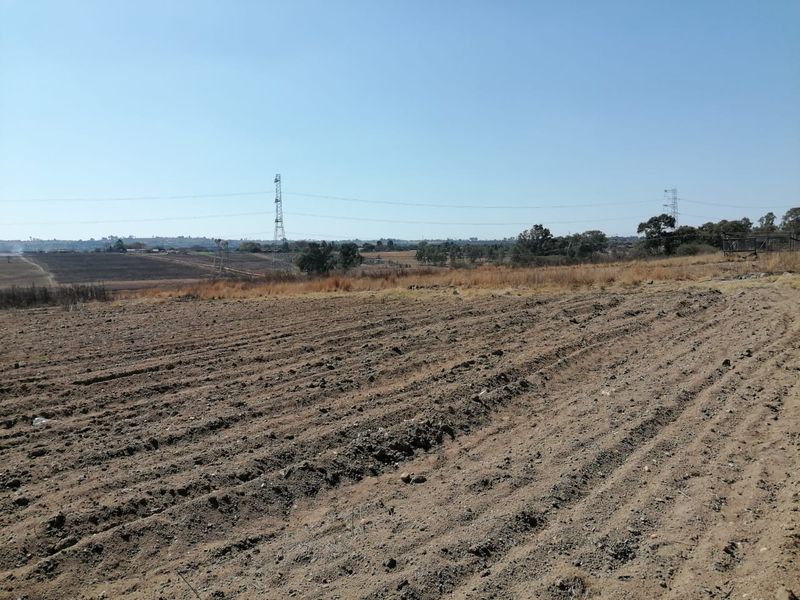 A wide-angle view of a vacant residential plot featuring cleared earth and distant power lines under a clear sky.