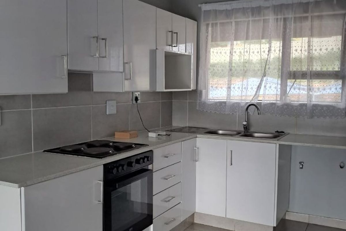 Modern kitchen featuring white cabinetry, stone countertops, built-in oven and hob, double sink, and neutral tiled flooring.