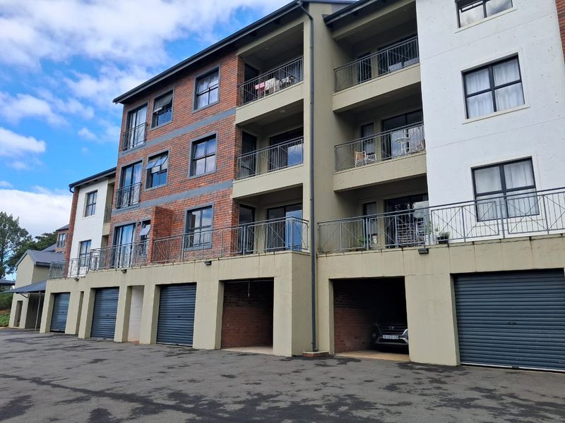 Exterior view of a multi-story apartment complex featuring brick and rendered facades, private balconies with metal railings, and ground-level garage access.
