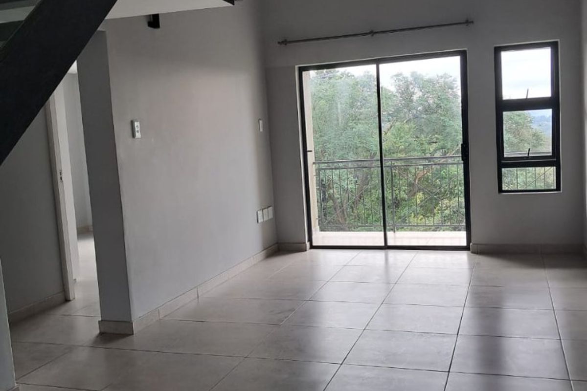 Spacious open-plan living area featuring neutral tiled flooring, a modern staircase with glass balustrade, and sliding doors leading to a balcony.
