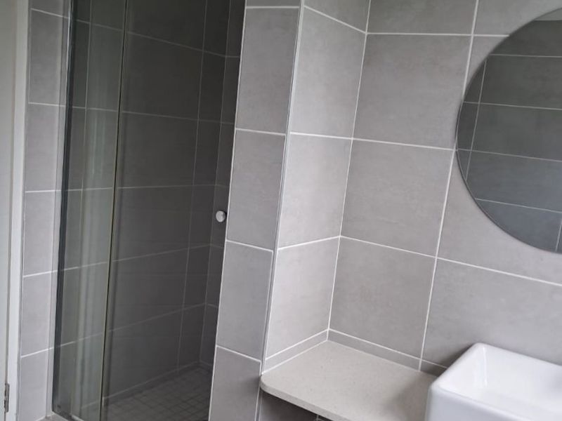 A modern bathroom featuring grey wall tiles, a glass shower enclosure, and a floating vanity shelf with a vessel sink.