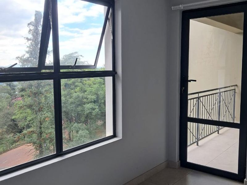 A bright, empty bedroom featuring neutral tiled flooring, modern aluminium window and door frames, and direct access to a private balcony.