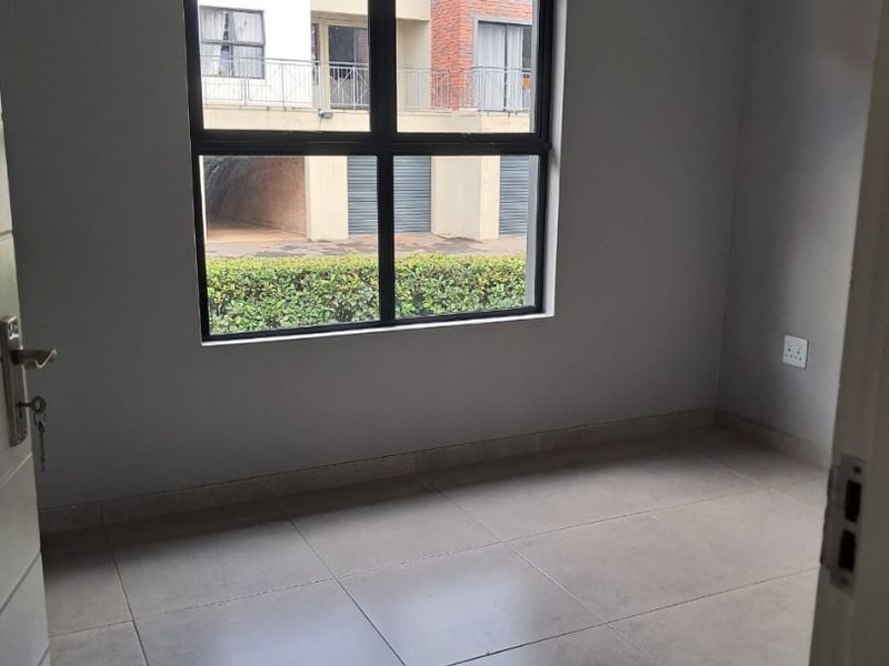 A clean, empty bedroom featuring neutral tiled flooring, grey walls, and a large aluminium-framed window providing natural light.
