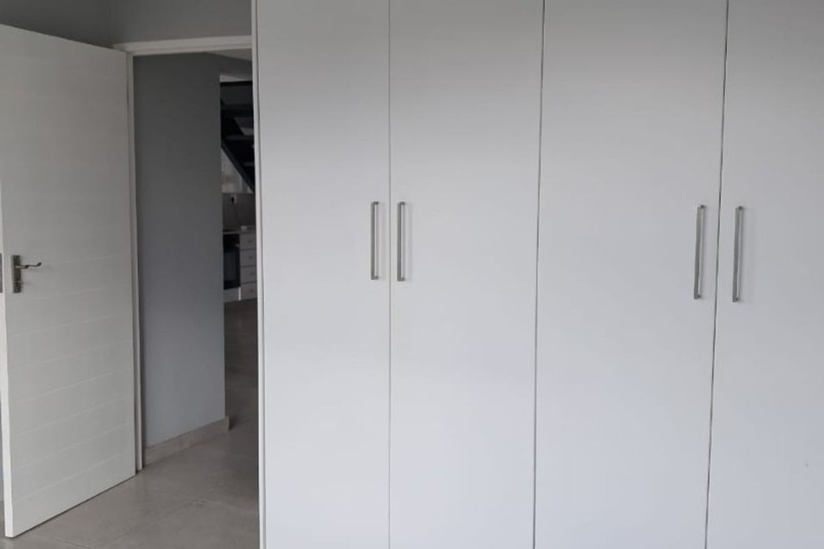 A clean, modern bedroom featuring neutral tiled flooring, recessed lighting, and ample built-in cupboard storage space.