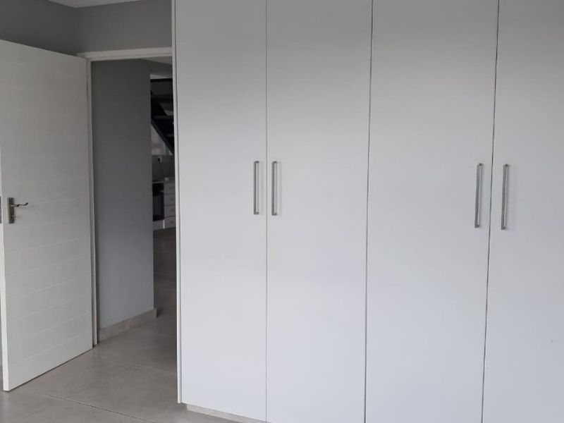 A clean, modern bedroom featuring neutral tiled flooring, recessed lighting, and ample built-in cupboard storage space.