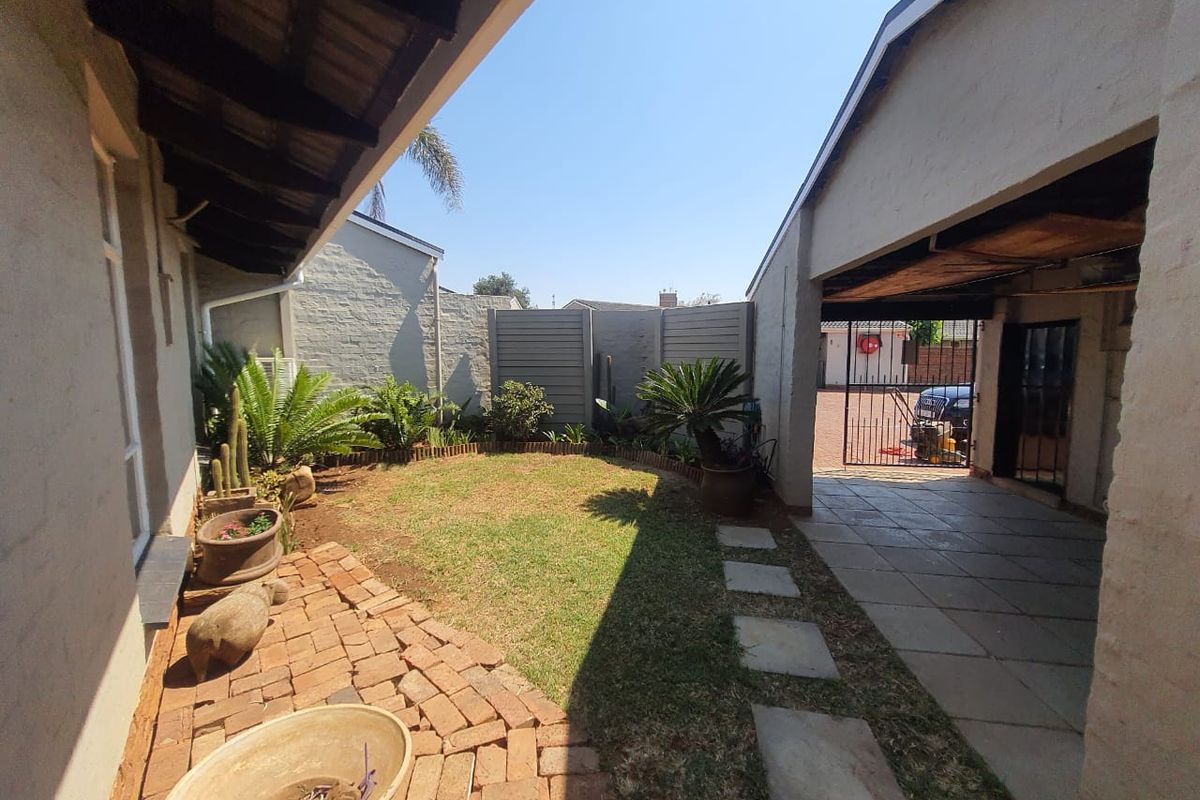 A private rear courtyard featuring a small lawn, brick and stone pathways, and a covered carport area with secure gated access.