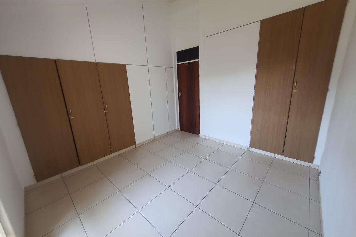 An empty bedroom featuring neutral tiled flooring and extensive built-in wooden cabinetry with white overhead storage panels.