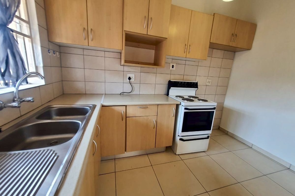Functional kitchen featuring light wood-look cabinetry, tiled backsplash, double stainless steel sink, and a freestanding electric stove.