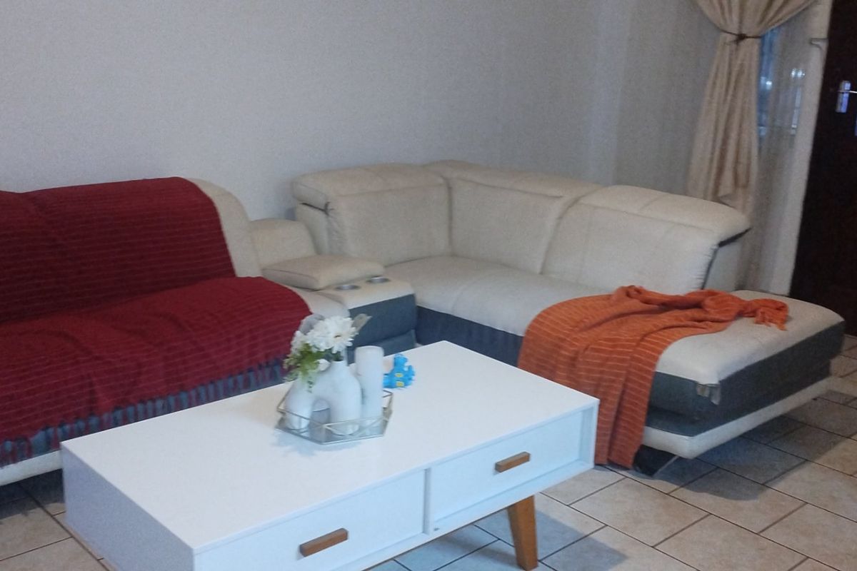 A living room area featuring tiled flooring and a timber entrance door, providing a functional space for relaxation.
