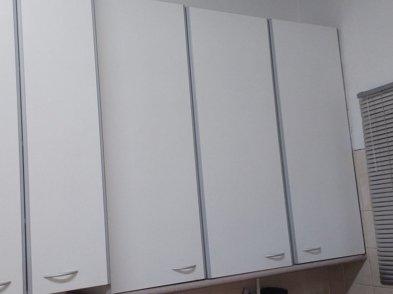 A view of white built-in kitchen cabinetry with modern handles and a window fitted with venetian blinds.