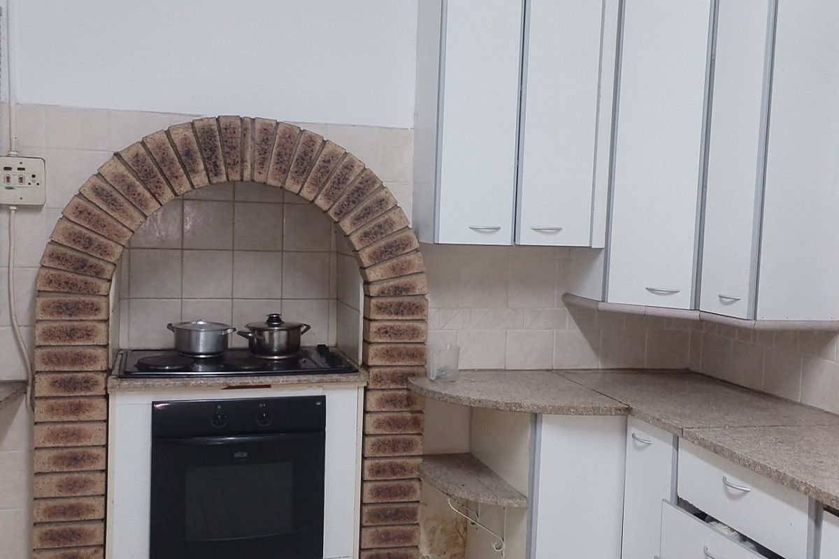 A functional kitchen featuring a distinctive brick arch over the built-in oven and hob, with laminate countertops and white cabinetry.