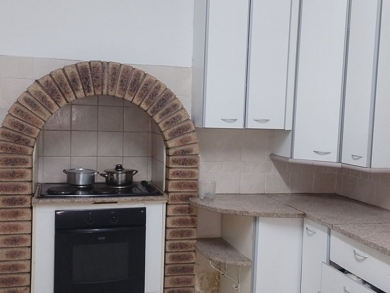A functional kitchen featuring a distinctive brick arch over the built-in oven and hob, with laminate countertops and white cabinetry.