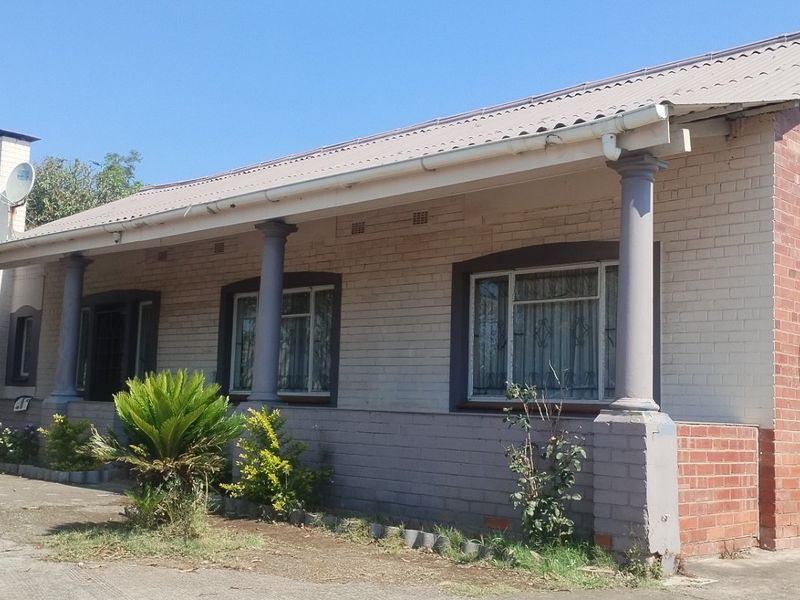 Front elevation of a single-story brick house featuring a covered veranda with support columns and security bars on the windows.