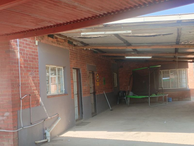 A covered outdoor patio area featuring brick walls, concrete flooring, and a corrugated metal roof structure in need of maintenance.