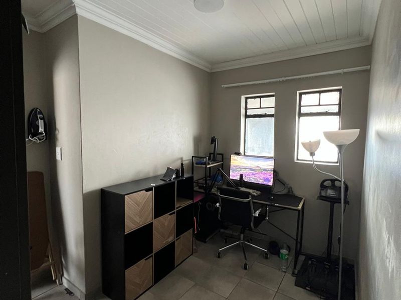 A compact home office featuring tiled flooring, a tongue and groove ceiling with crown molding, and dual windows providing natural light.