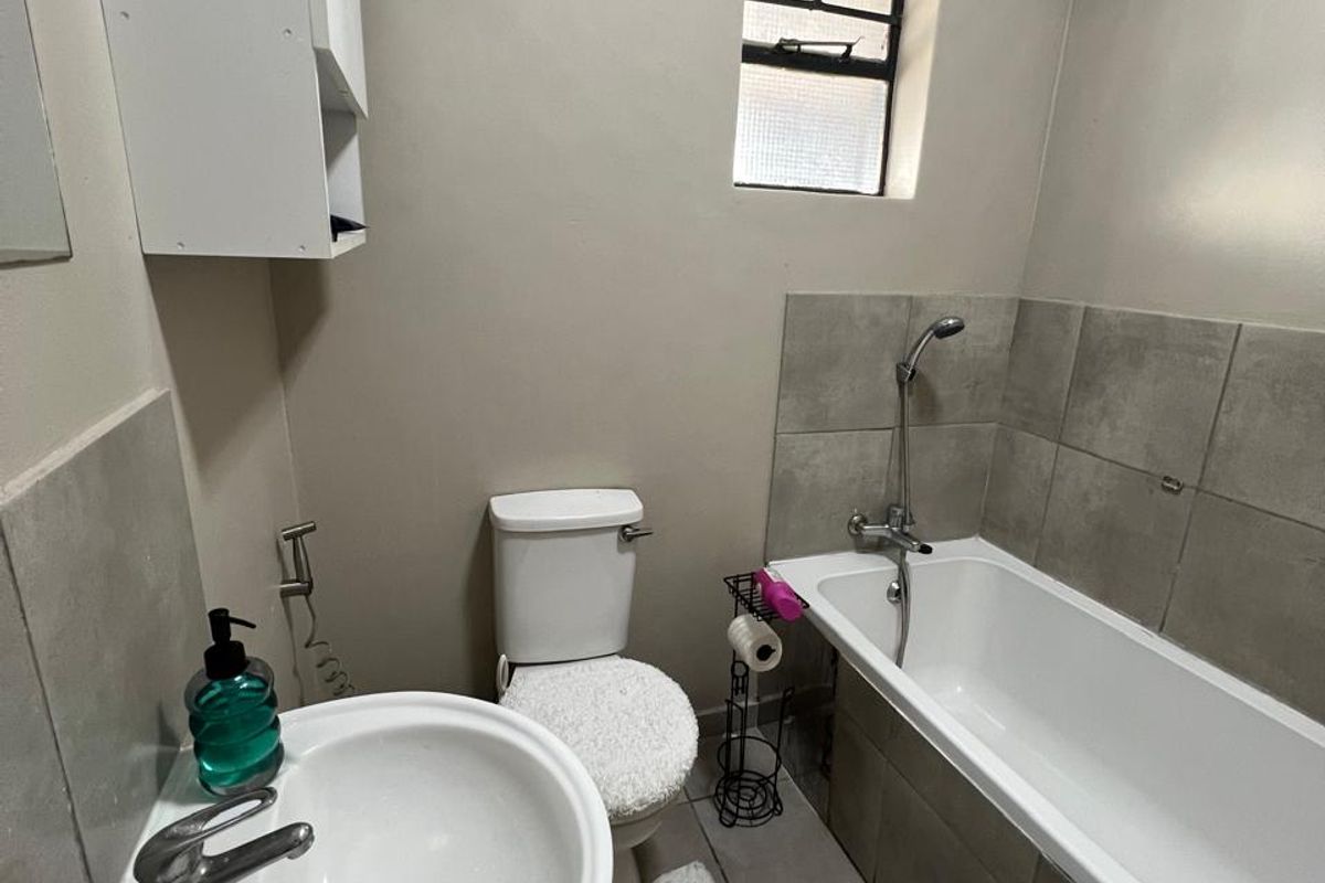 A functional bathroom featuring a pedestal basin, toilet, and a bathtub with a shower mixer, finished with neutral wall paint and tiled flooring.