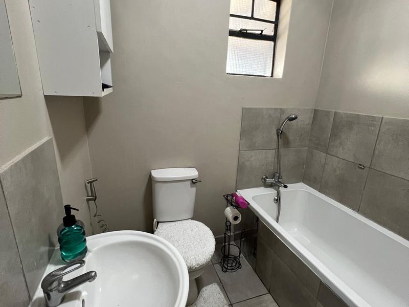 A functional bathroom featuring a pedestal basin, toilet, and a bathtub with a shower mixer, finished with neutral wall paint and tiled flooring.