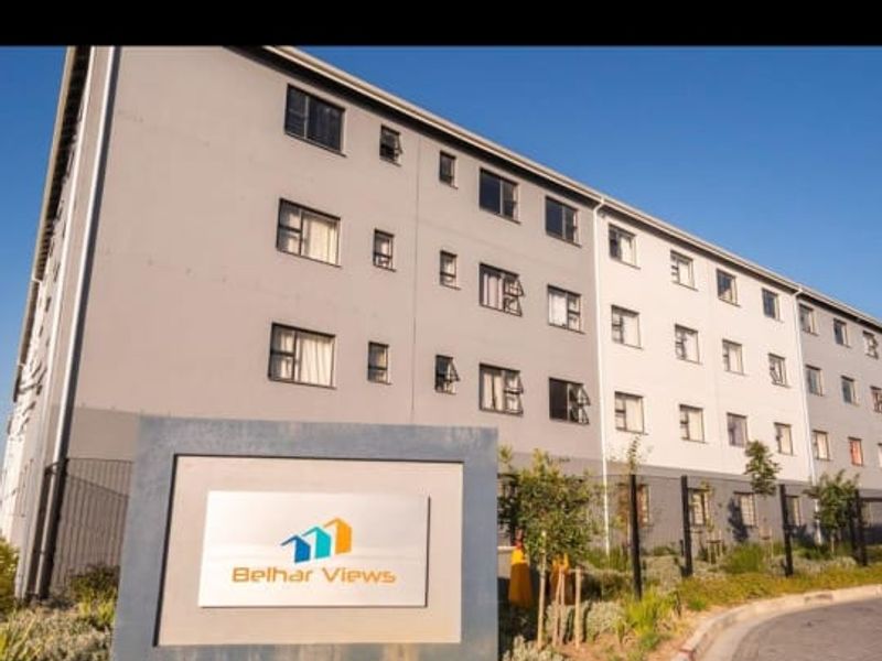 Exterior view of the Belhar Views apartment complex, featuring a paved entrance, security fencing, and landscaped garden beds.