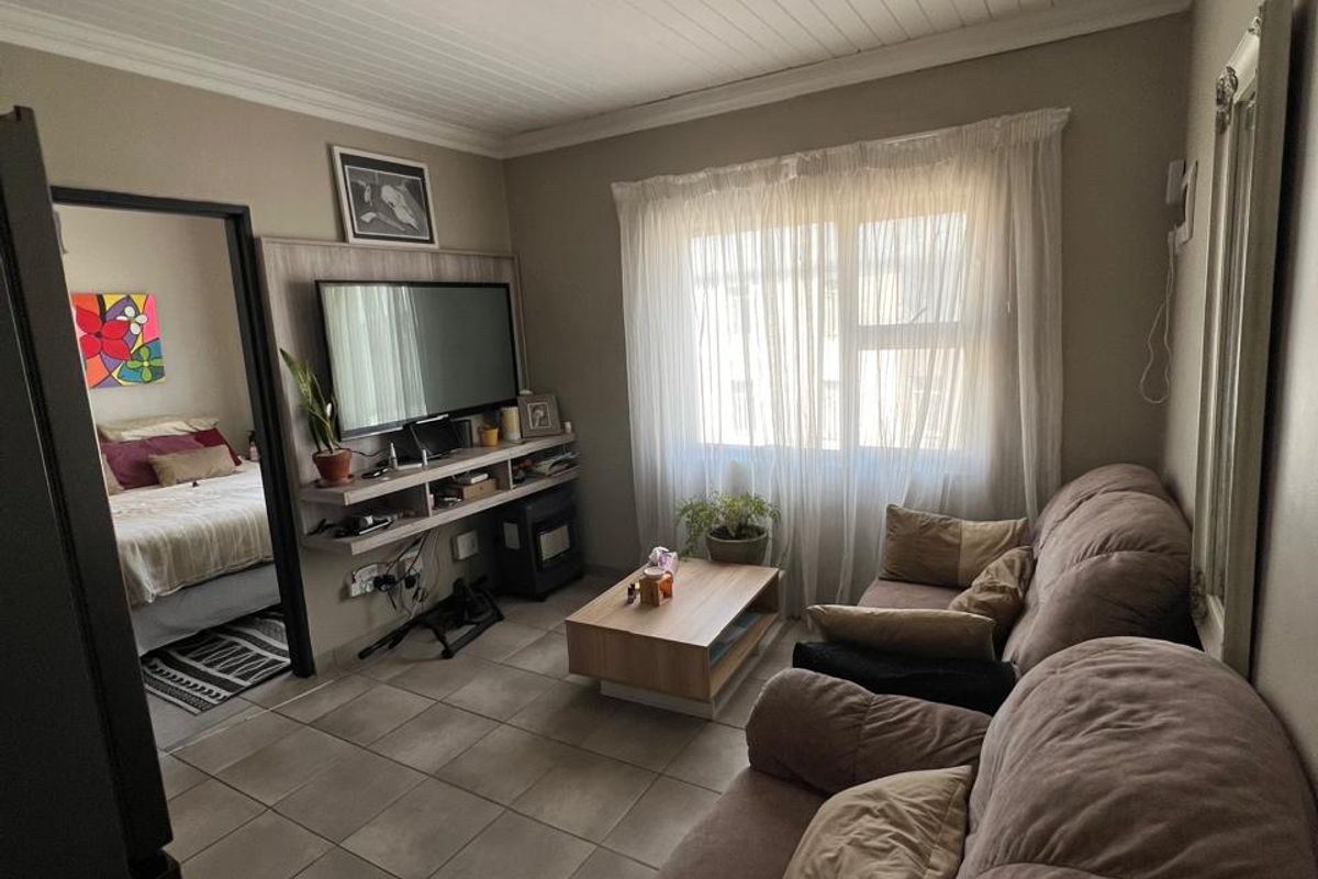 A cozy living room featuring tiled flooring, a tongue and groove ceiling, and a built-in media console, with an adjacent bedroom visible.