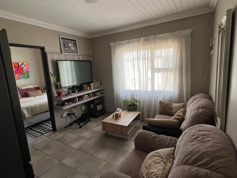 A cozy living room featuring tiled flooring, a tongue and groove ceiling, and a built-in media console, with an adjacent bedroom visible.