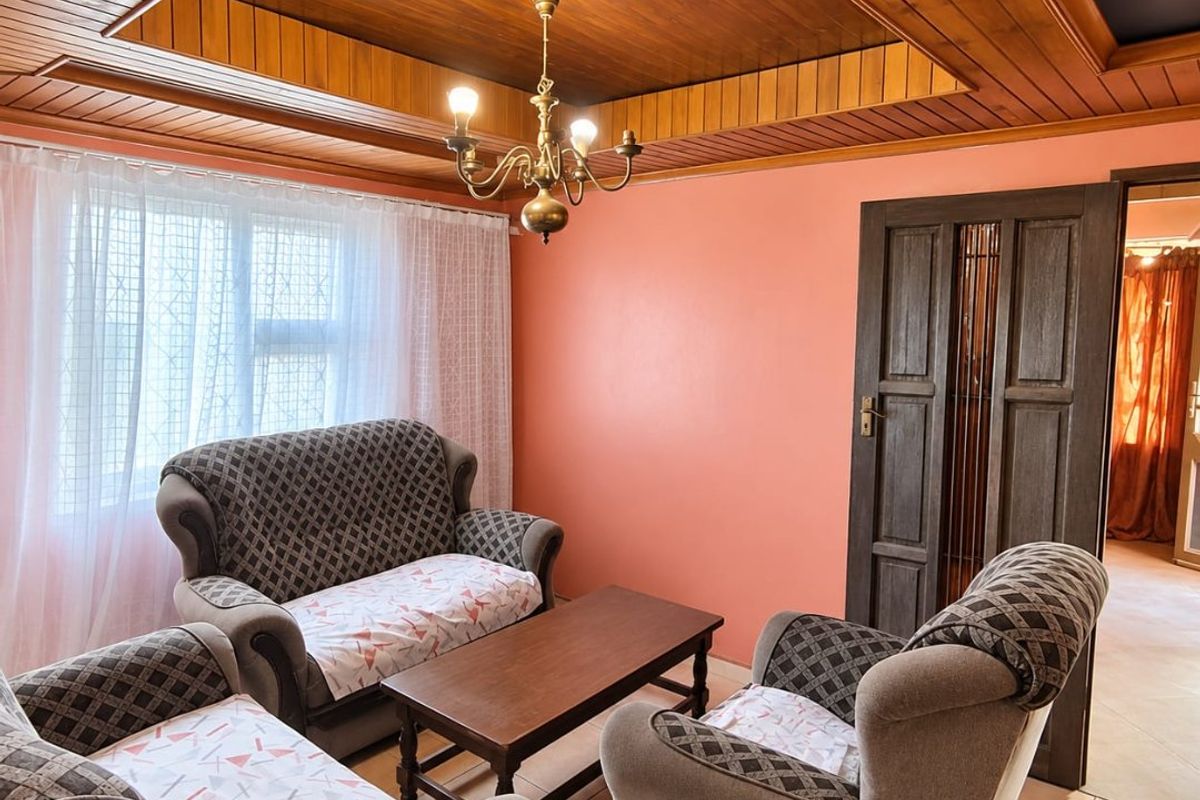 A living room featuring a distinctive timber tongue and groove tray ceiling, tiled flooring, and a classic timber panelled door.