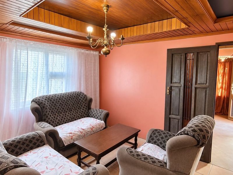A living room featuring a distinctive timber tongue and groove tray ceiling, tiled flooring, and a classic timber panelled door.