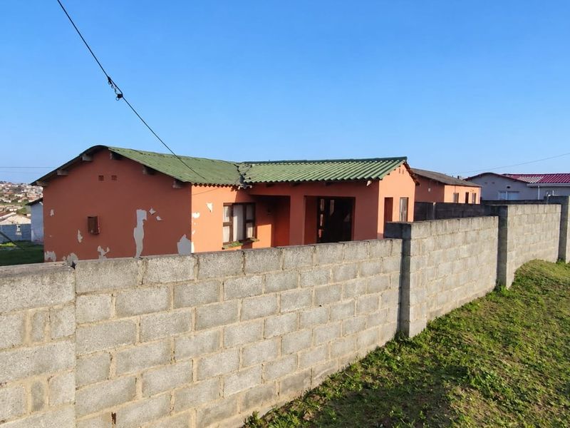 Front view of a single-story house featuring a corrugated metal roof, covered entrance, and a concrete block boundary wall requiring exterior maintenance.