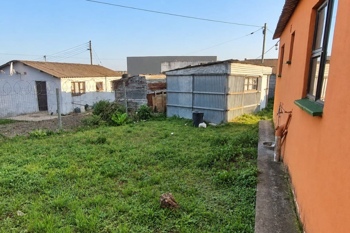 Rear garden area featuring a lawn, concrete pathway, and a corrugated metal outbuilding, enclosed by wire fencing.