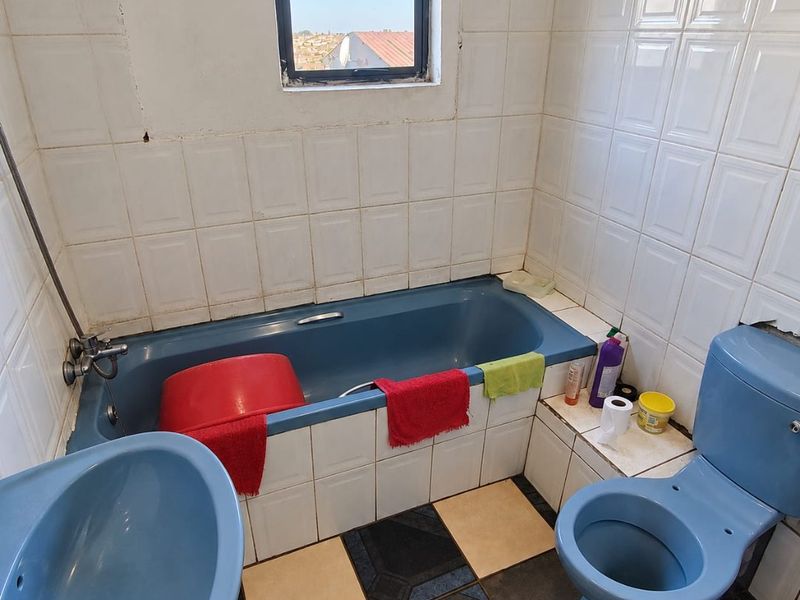 A dated bathroom featuring blue sanitaryware, tiled walls, and a checkered floor, requiring modernization and cosmetic updates to improve its overall condition.