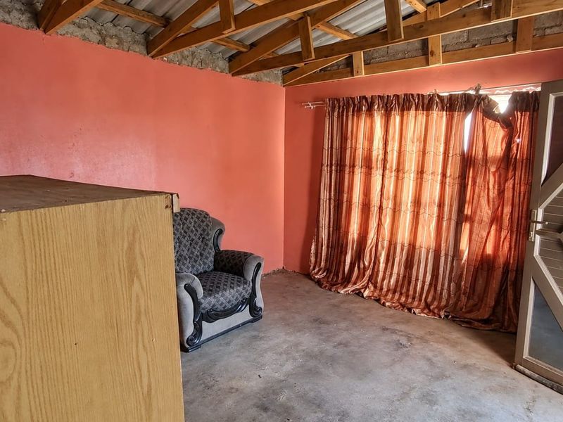 A rustic living area featuring exposed timber roof trusses, corrugated metal roofing, and a concrete floor, offering a blank canvas for renovation.